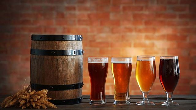 A photo of four glasses filled with craft beers next to a keg