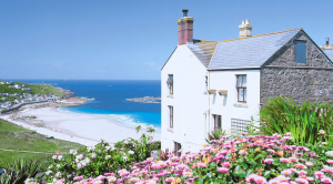 Coastal cottage with flowers in the foreground and a sandy beach in the background