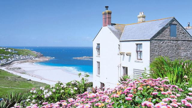 Coastal cottage with flowers in the foreground and a sandy beach in the background
