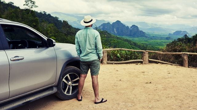 Man standing by car in a sunhat looking at the view
